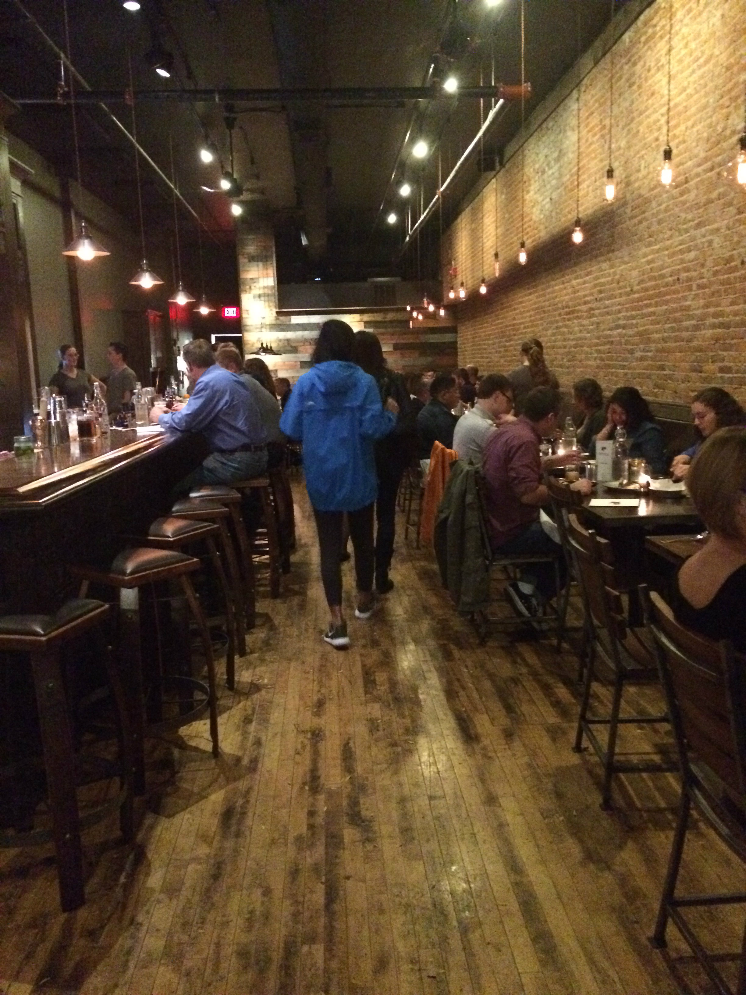 An aisle with eople at tables on either side; vintage brick walls and a wooden floor line the room.