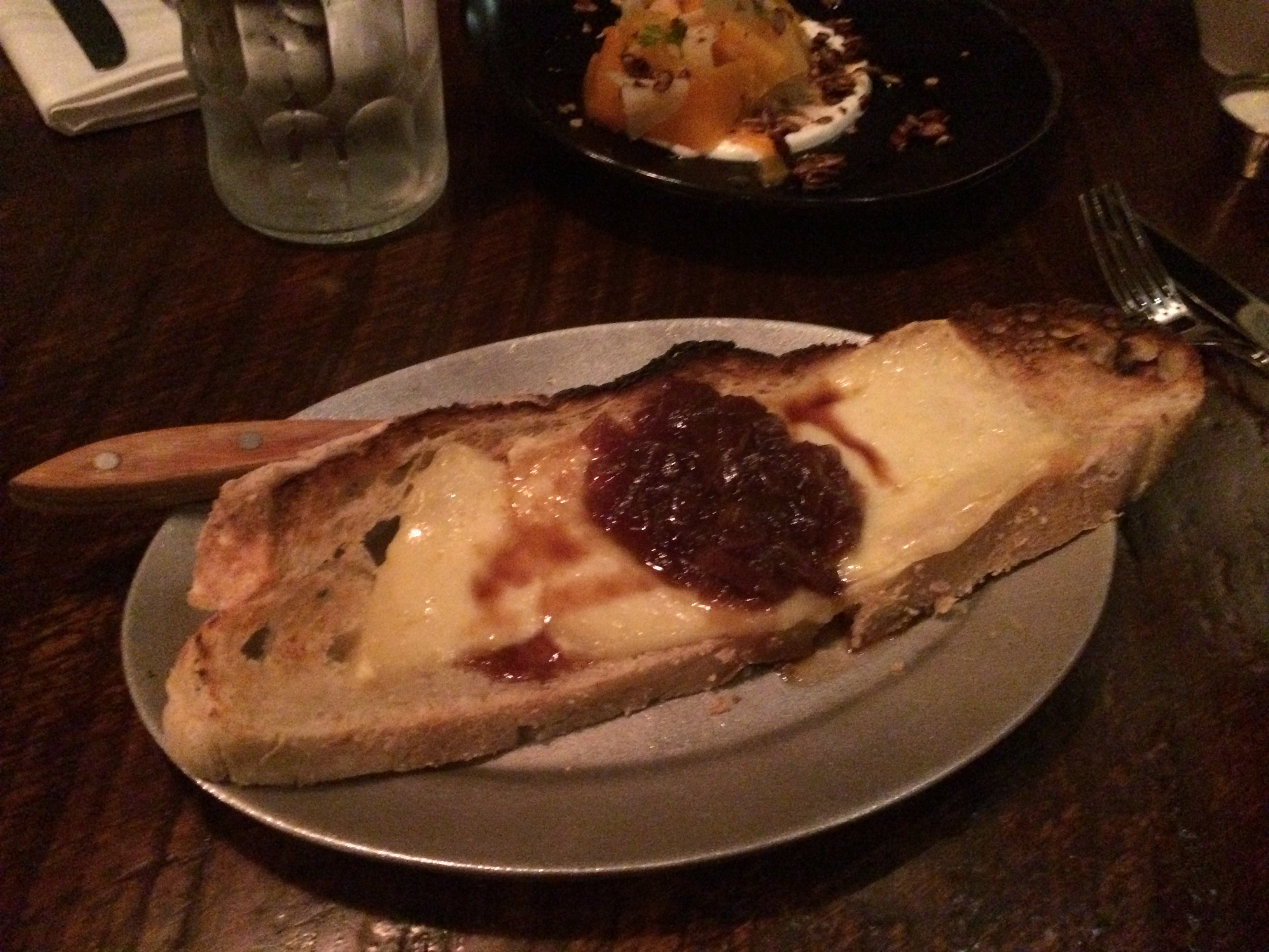 A long peice of bread with gooey, baked cheese, topped with jam