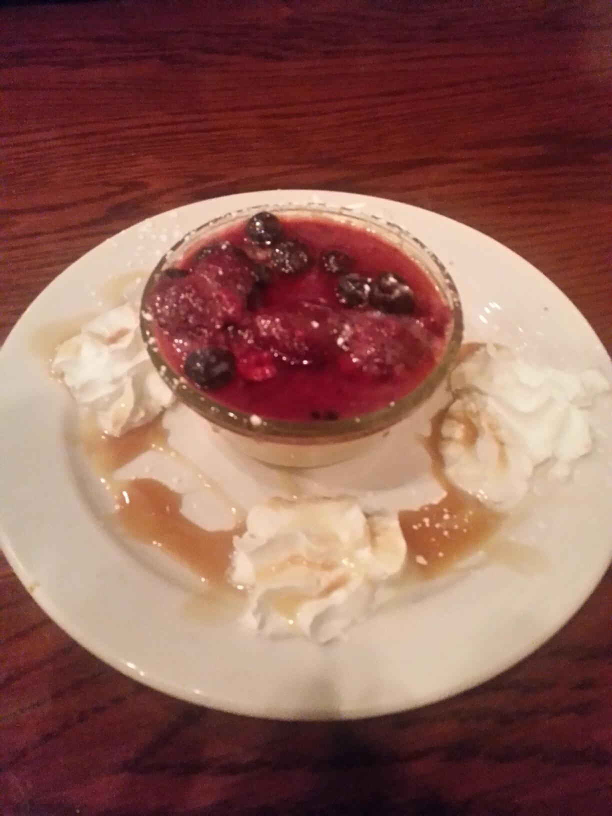 A small bowl of creme brulee topped with mixed berries, surrounded by dollops of whipped cream