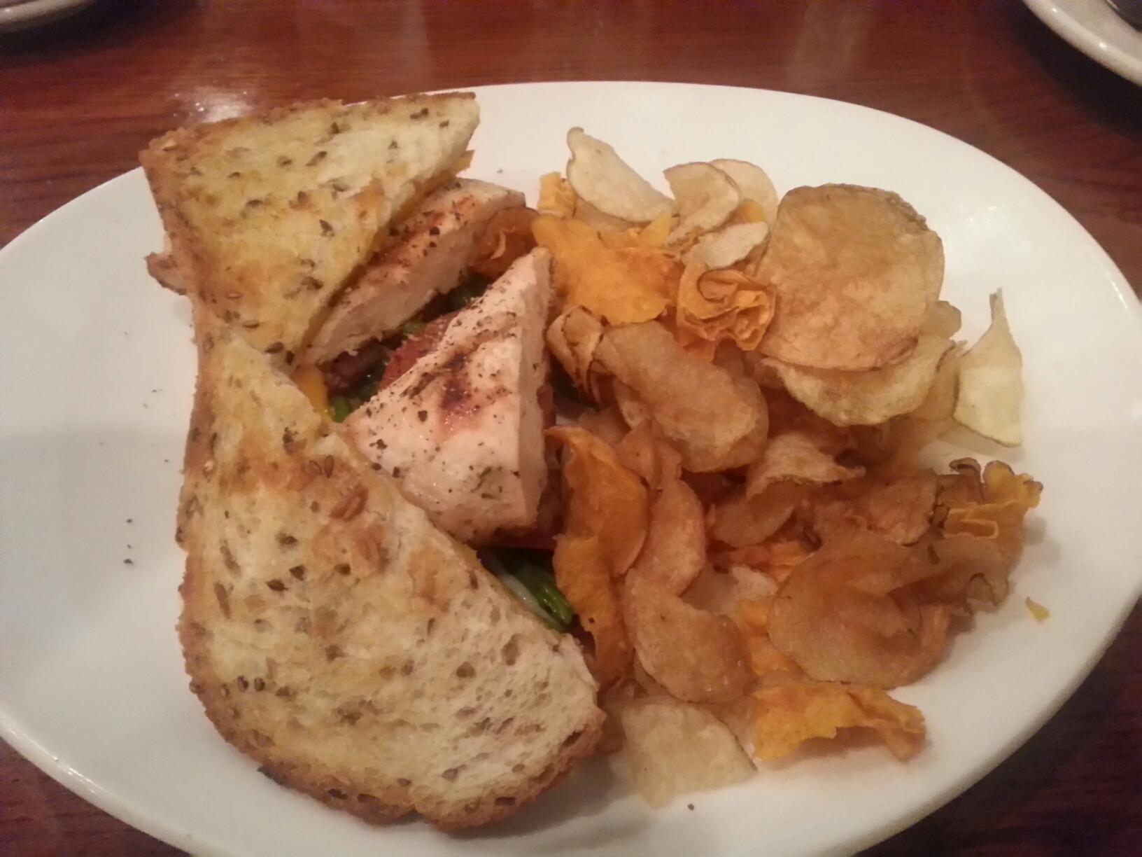 A salmon blt cut in half, with a side of chips