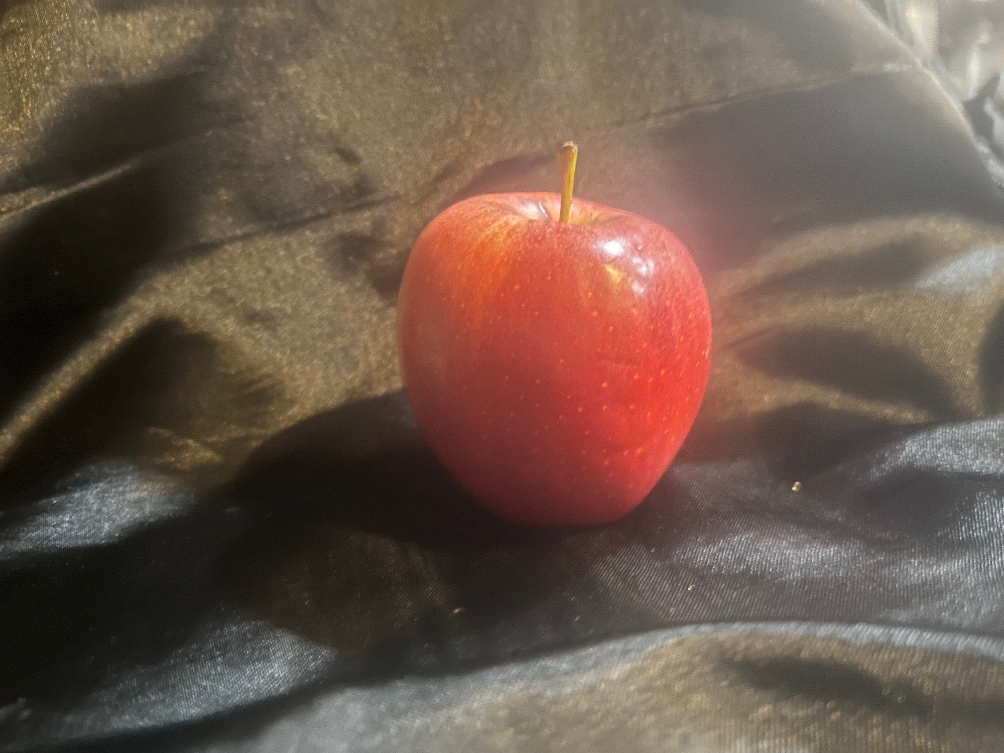 Photograph of an apple against a black background. The highlights from the apple are reflected onto the background, making it seem a gray-ish yellow.