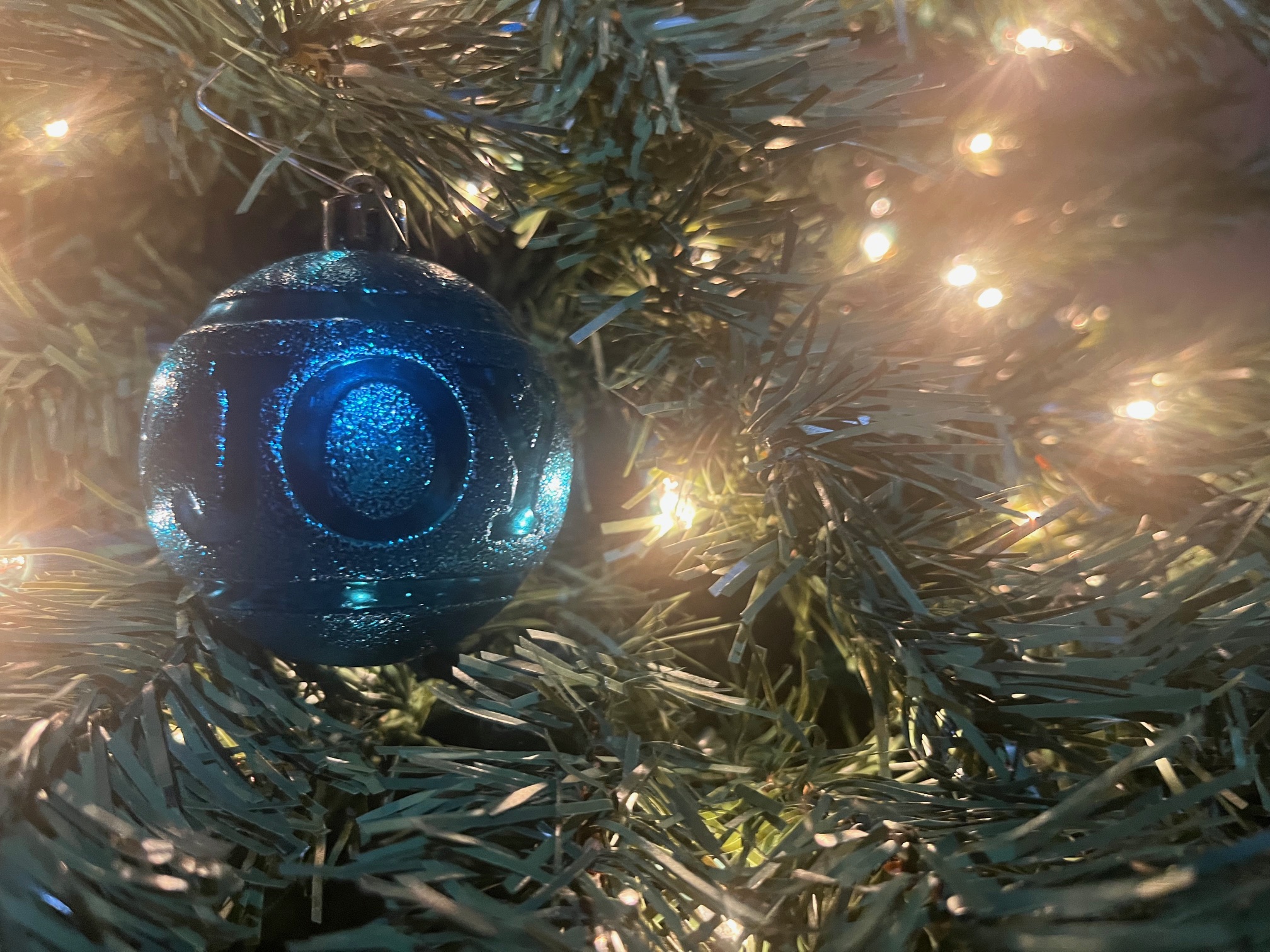 Close-up image of a Christmas ornament on a Christmas tree with lights. The ornament is on the left side of the photograph, and the lights are on the right.