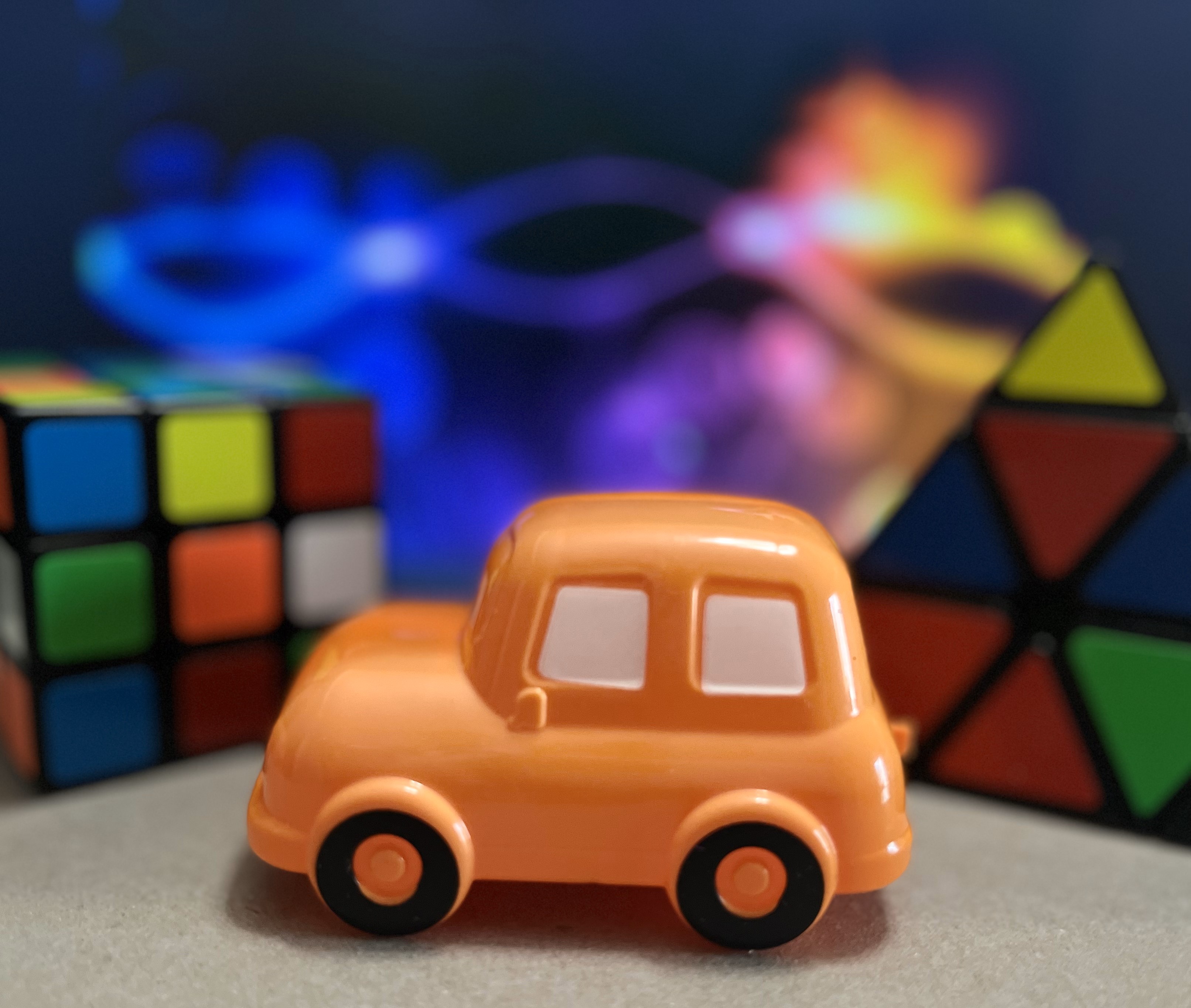 picture of a toy car with unsolved rubiks puzzles in the background along with a colorful curved (but blurred) background.