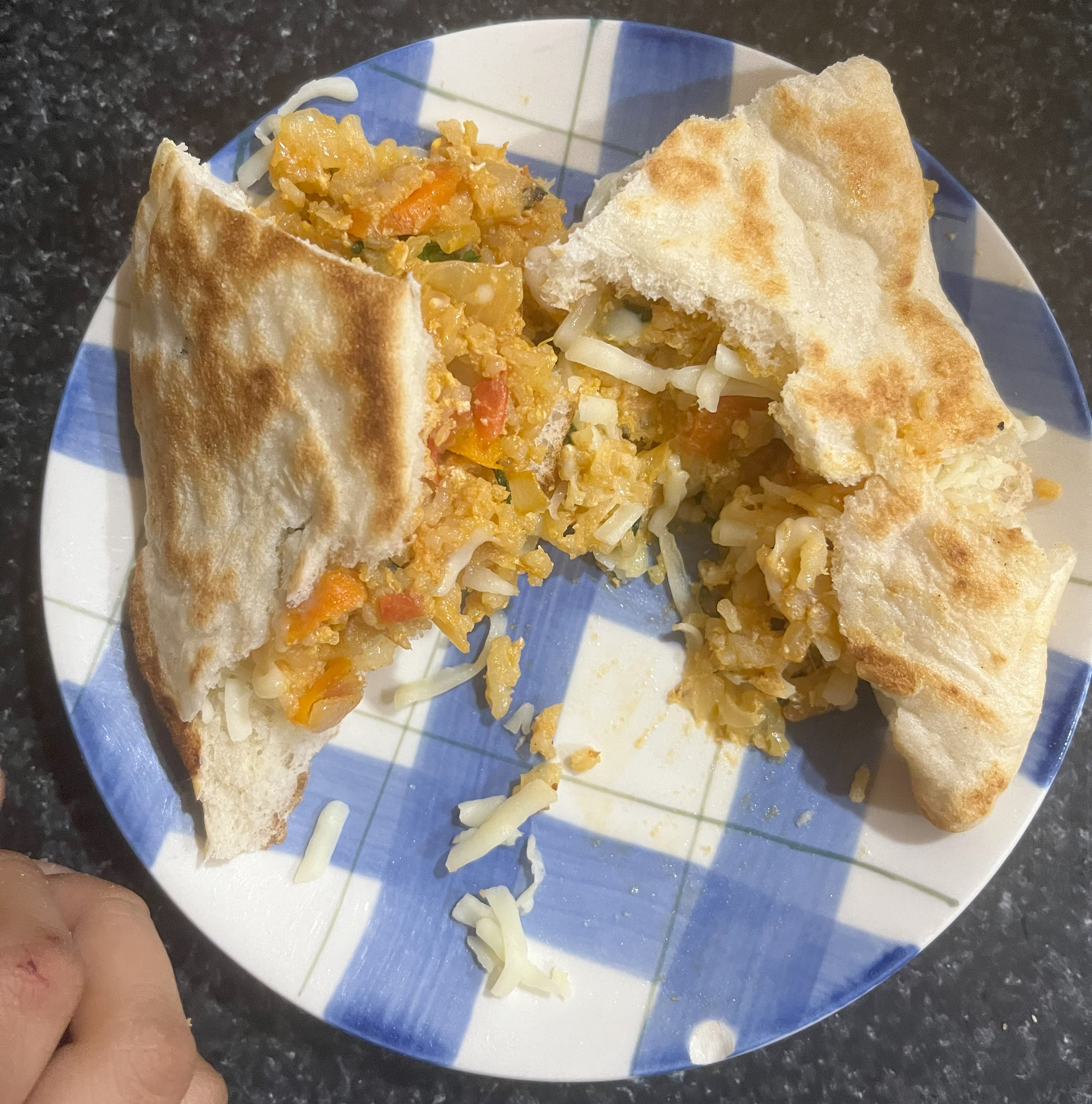 Photograph of egg sandwich on a blue and white plate. The plate is on a black granite table and a portion of a hand can be seen.