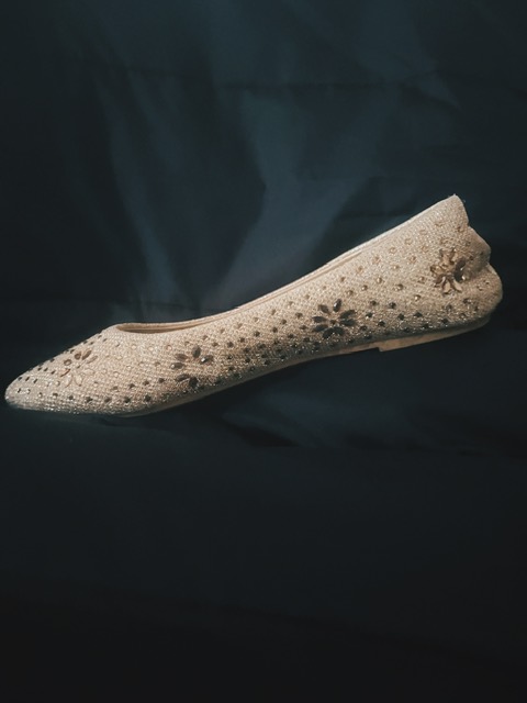 Golden slipper with beads arranged in the shape of flowers on a black background.