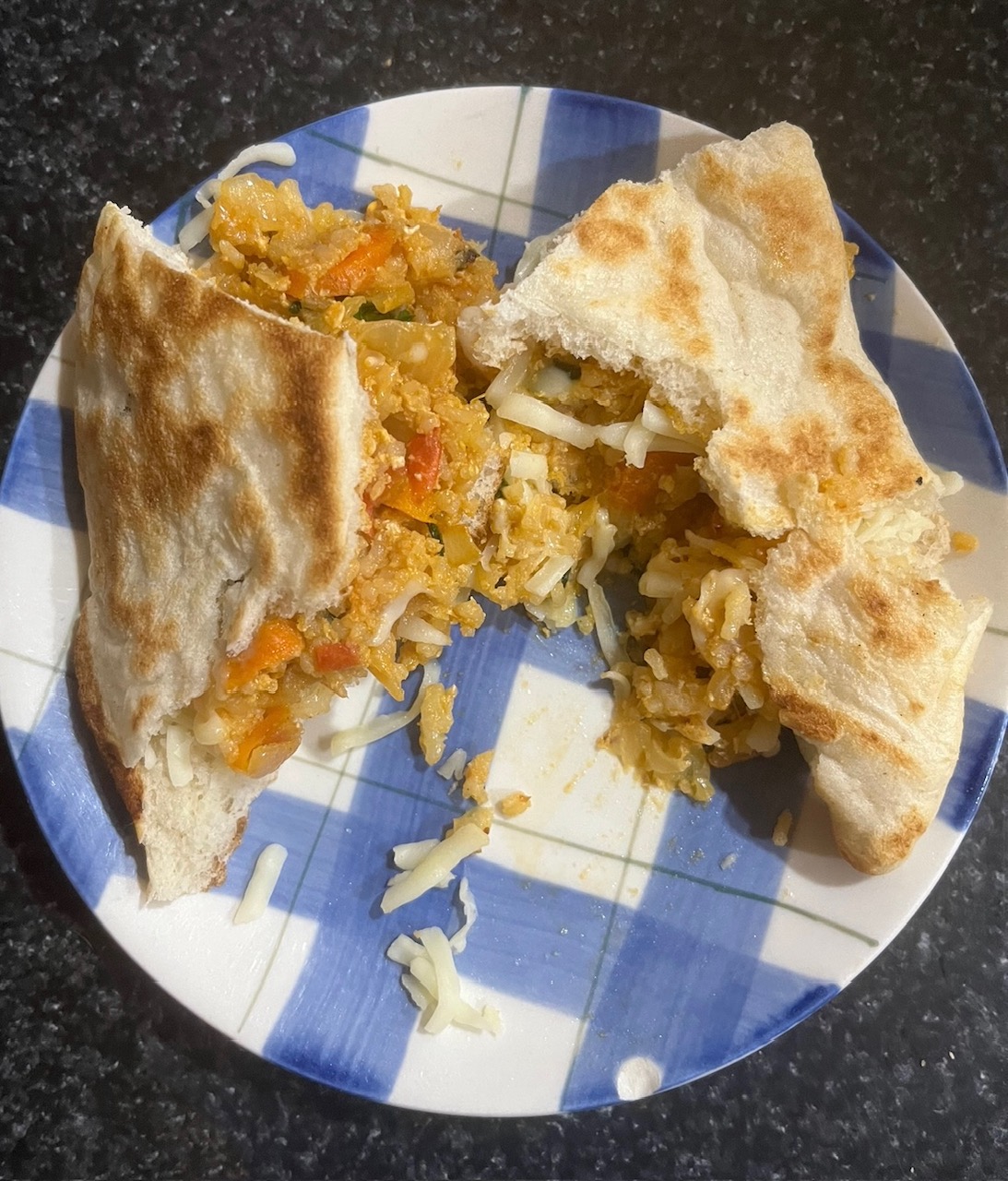 Image of an egg sandwich in pita bread on a blue checked plate.