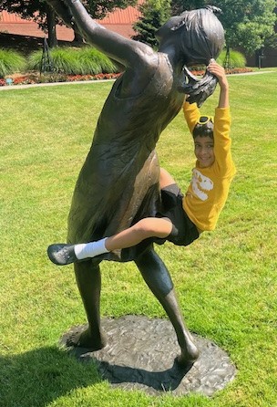 A small in a yellow shirt boy playfully hanging from a statue.